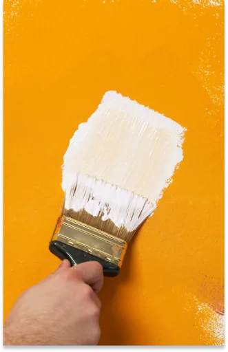 Pinsel mit weißer Farbe auf gelber Wand
